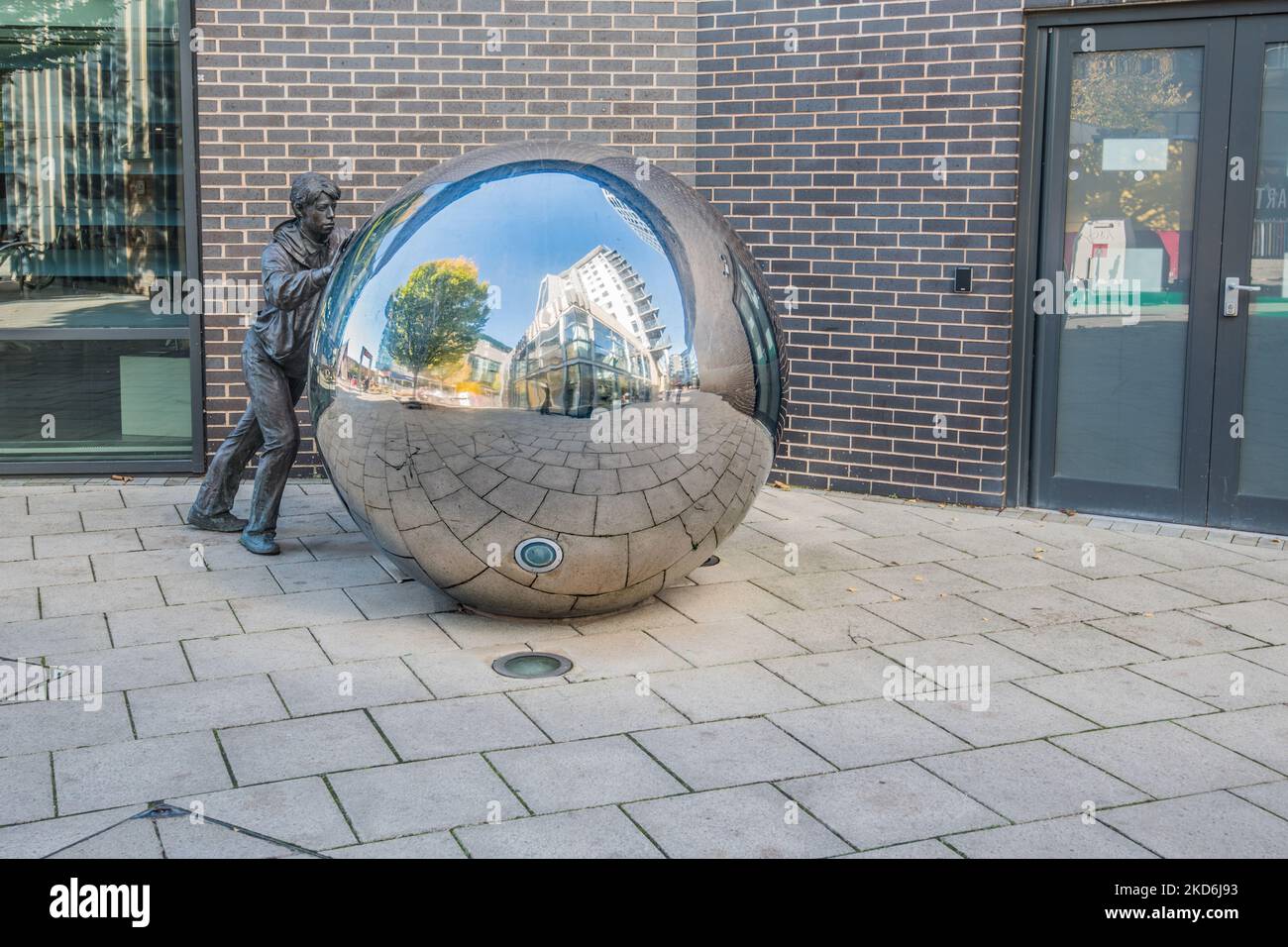 Scultura in , area di Leeds Dock, che mostra una delle due figure in bronzo a grandezza naturale che spingono una sfera a specchio in acciaio inossidabile. Foto Stock