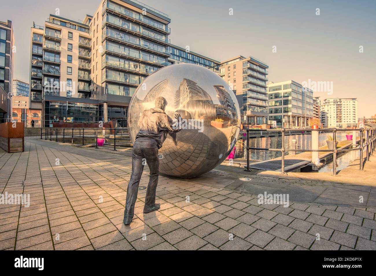 Arte pubblica al Leeds Dock con una palla specchiata che viene spinta avanti. Scultura nel New Dock precedentemente Clarence Dock, Leeds, che mostra una figura di bronzo a grandezza naturale. Foto Stock