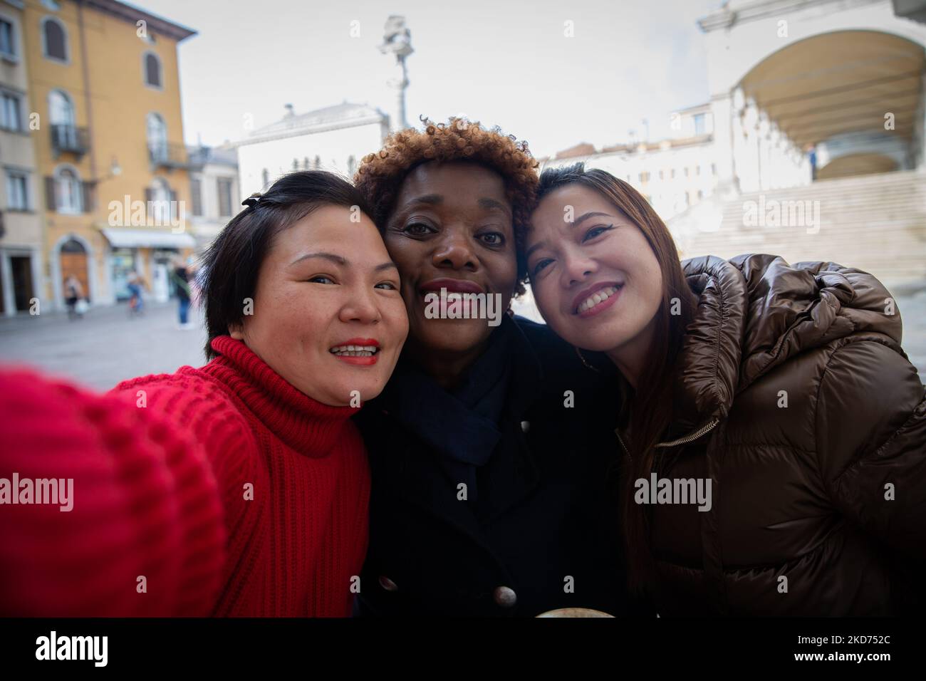 Tre simpaticissimi amici sorridenti e diversi prendono selfie durante la loro passeggiata nel centro della città. Foto Stock