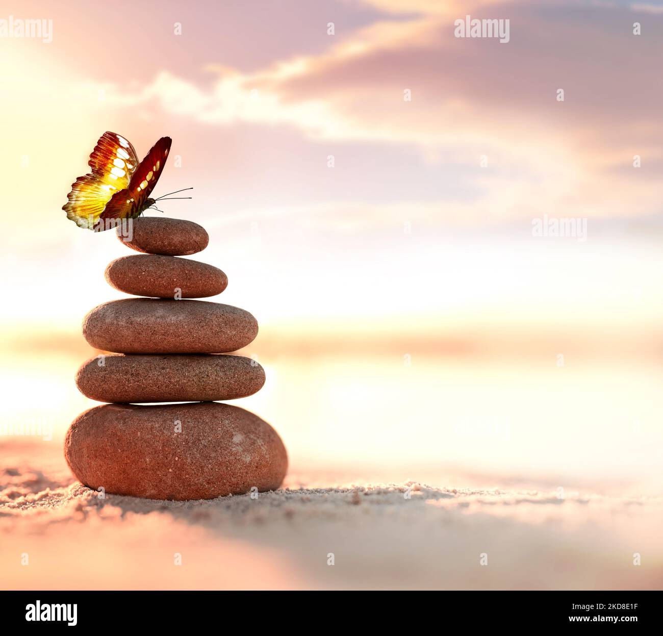 Equilibrata piramide di ciottoli e farfalla sulla spiaggia. Abstract caldo tramonto bokeh con sabbia sullo sfondo. Pietre Zen sulla spiaggia di mare, equilibrio conce Foto Stock