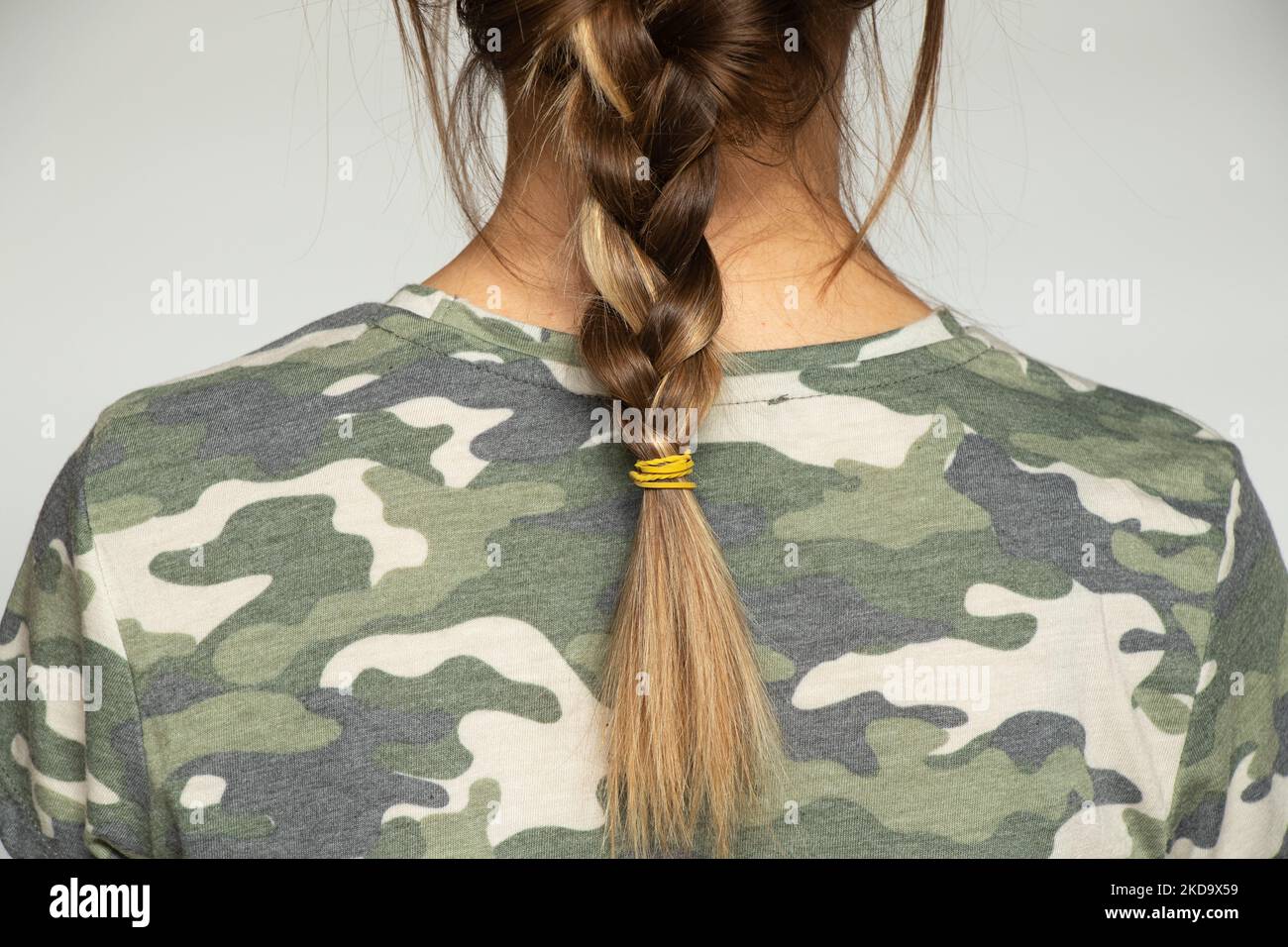 Ragazza in uniforme mimetica verde militare con scythe su sfondo isolato, vista posteriore, donna soldato Foto Stock