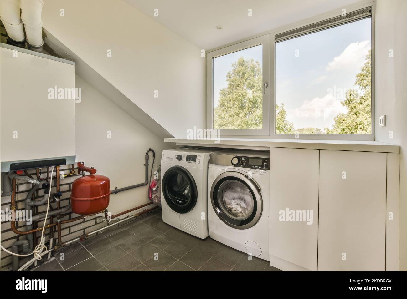 Locale caldaia di un edificio di appartamenti con tubi e dosatori. Una lunga sala con comunicazioni ingegneristiche e lavatrice Foto Stock