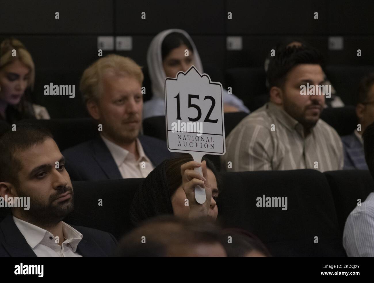 Una donna iraniana solleva il suo segno di offerta in una sala d'asta durante l'asta del 7th Art of the Islamic and Iranian Worlds Auction, tenuta dalla Melli (National) Auction House in un centro conferenze nel nord di Teheran il 24 giugno 2022. (Foto di Morteza Nikoubazl/NurPhoto) Foto Stock