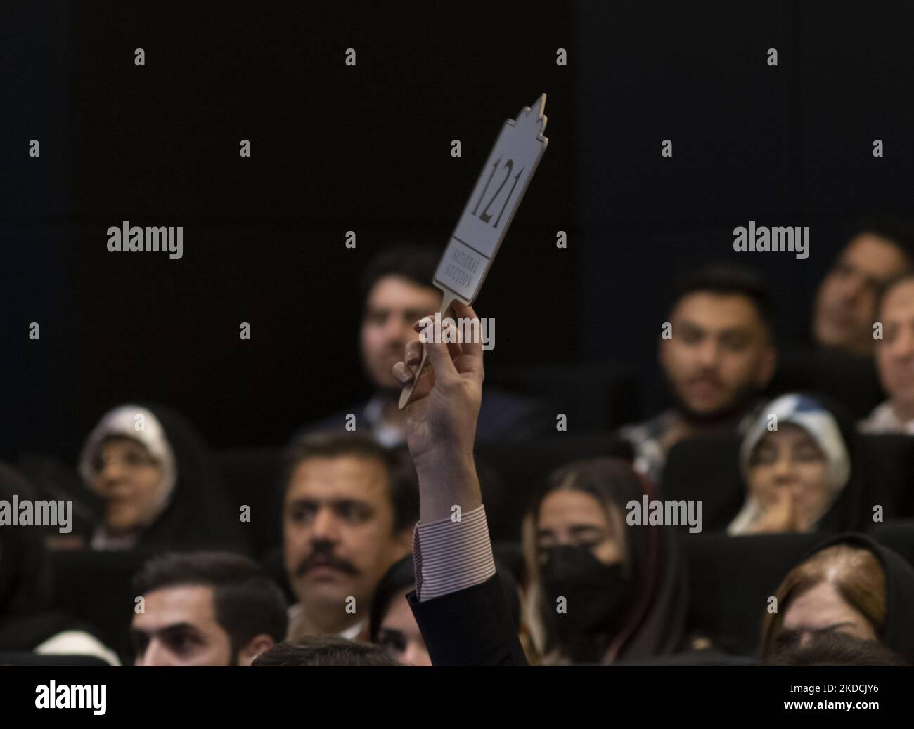 Un uomo iraniano solleva il suo segno di offerta in una sala d'asta durante l'asta del 7th Art of the Islamic and Iranian Worlds Auction, tenuta dalla Melli (National) Auction House in un centro conferenze nel nord di Teheran il 24 giugno 2022. (Foto di Morteza Nikoubazl/NurPhoto) Foto Stock