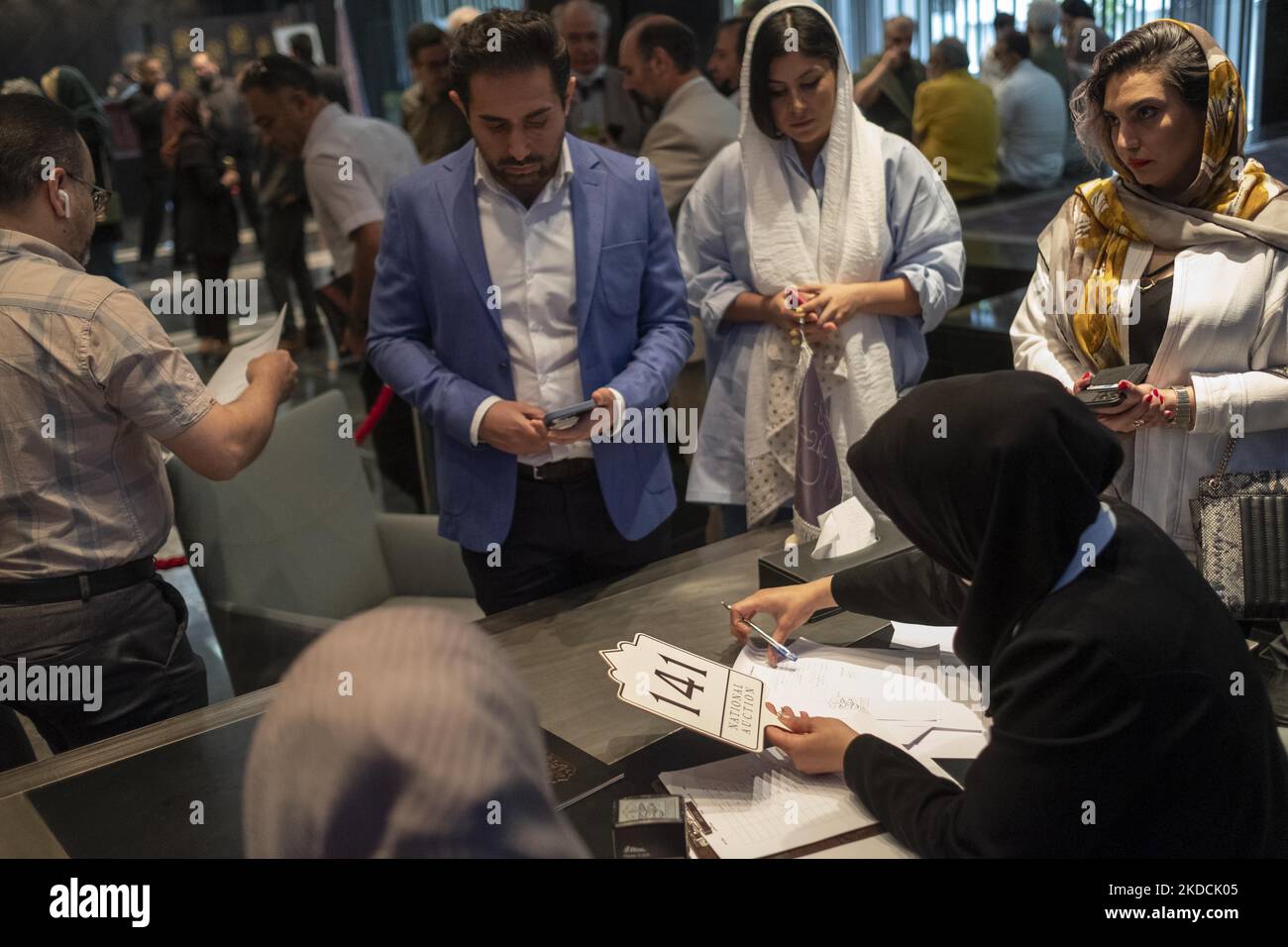 La gente iraniana aspetta di ricevere un'offerta d'asta mentre si registra all'asta durante l'asta del 7th Art of the Islamic and Iranian Worlds Auction, tenuta dalla Melli (National) Auction House in un centro conferenze nel nord di Teheran il 24 giugno 2022. (Foto di Morteza Nikoubazl/NurPhoto) Foto Stock