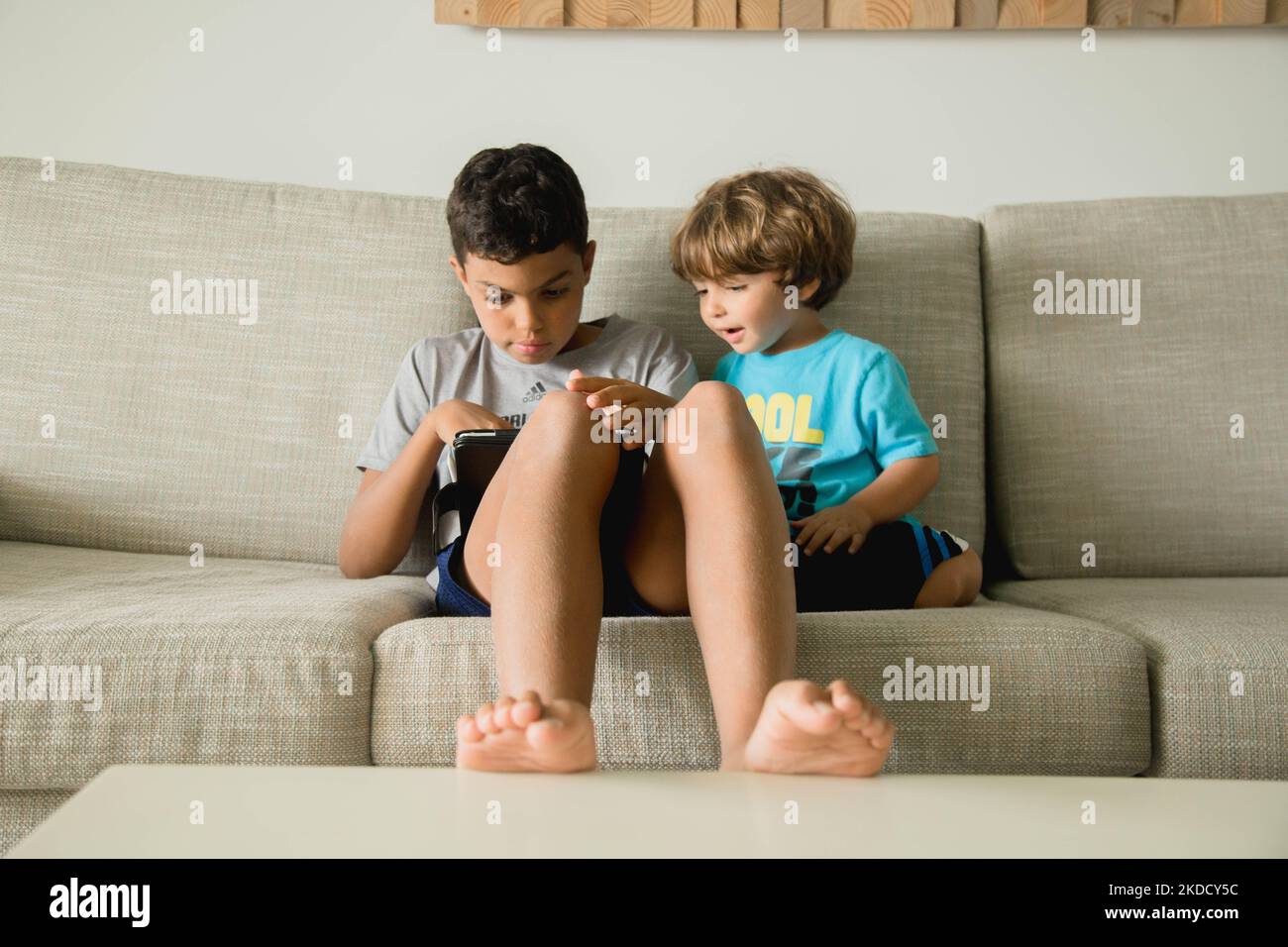 Due fratelli che giocano a vide mentre si siedono sul divano Foto Stock