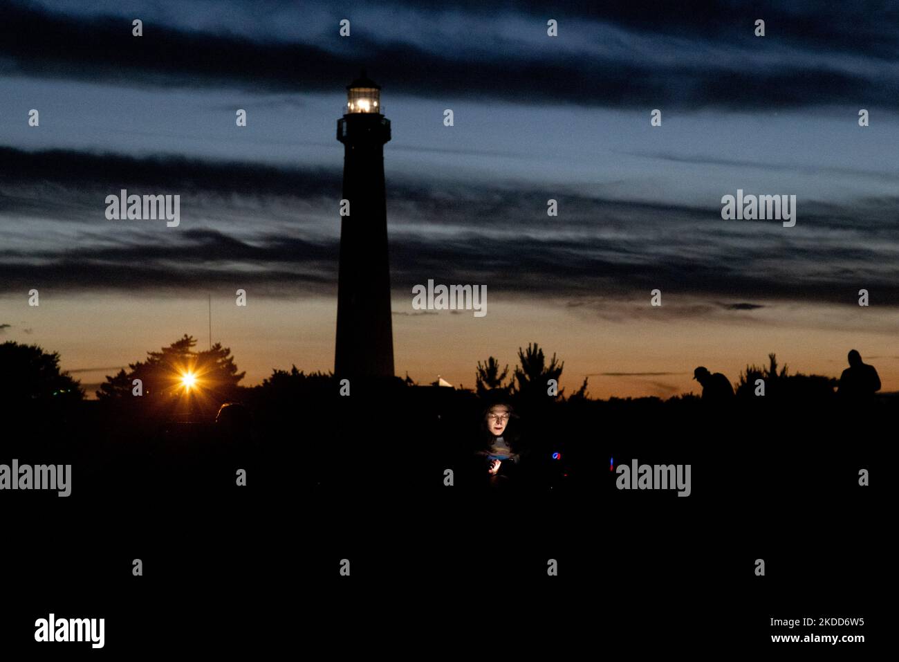 Una donna guarda il suo telefono sulla spiaggia vicino al faro di Cape May a Cape May Point, New Jersey al tramonto il 4 luglio 2022 (Foto di Bryan Olin Dozier/NurPhoto) Foto Stock