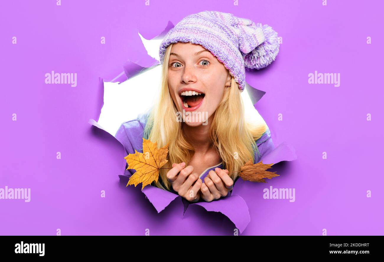 Modello sorpreso in cappello lavorato a maglia con foglie autunnali che guardano attraverso la carta. Vendita autunnale. Foto Stock