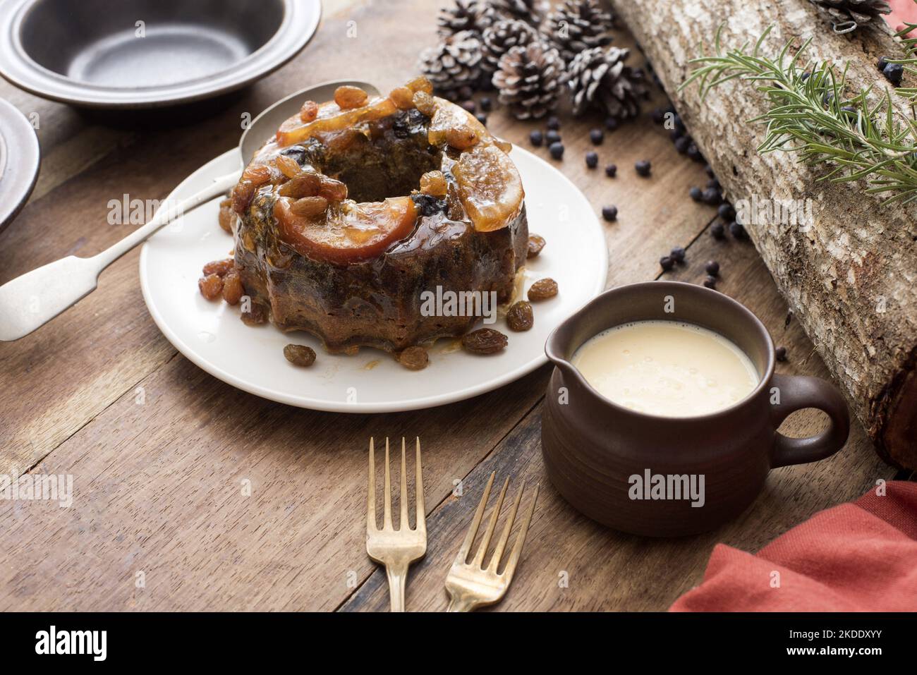 Budino di prugna con crema di brandy o salsa pronta per essere servita per dessert di Natale su un tavolo di legno decorato Foto Stock