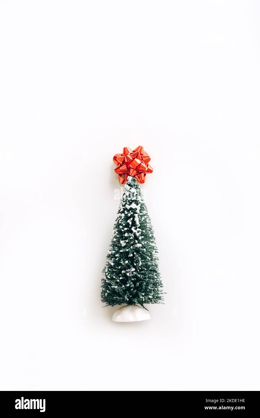 Bel mini albero di Natale artificiale con arco rosso in cima su sfondo bianco. Piccolo albero di Natale Foto Stock