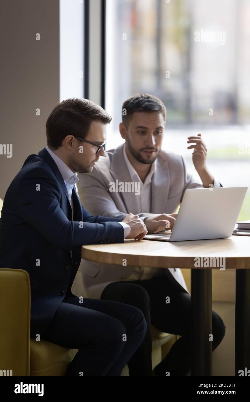 Due giovani colleghi dell'ufficio 35s discutono di un progetto on-line che utilizza il laptop Foto Stock