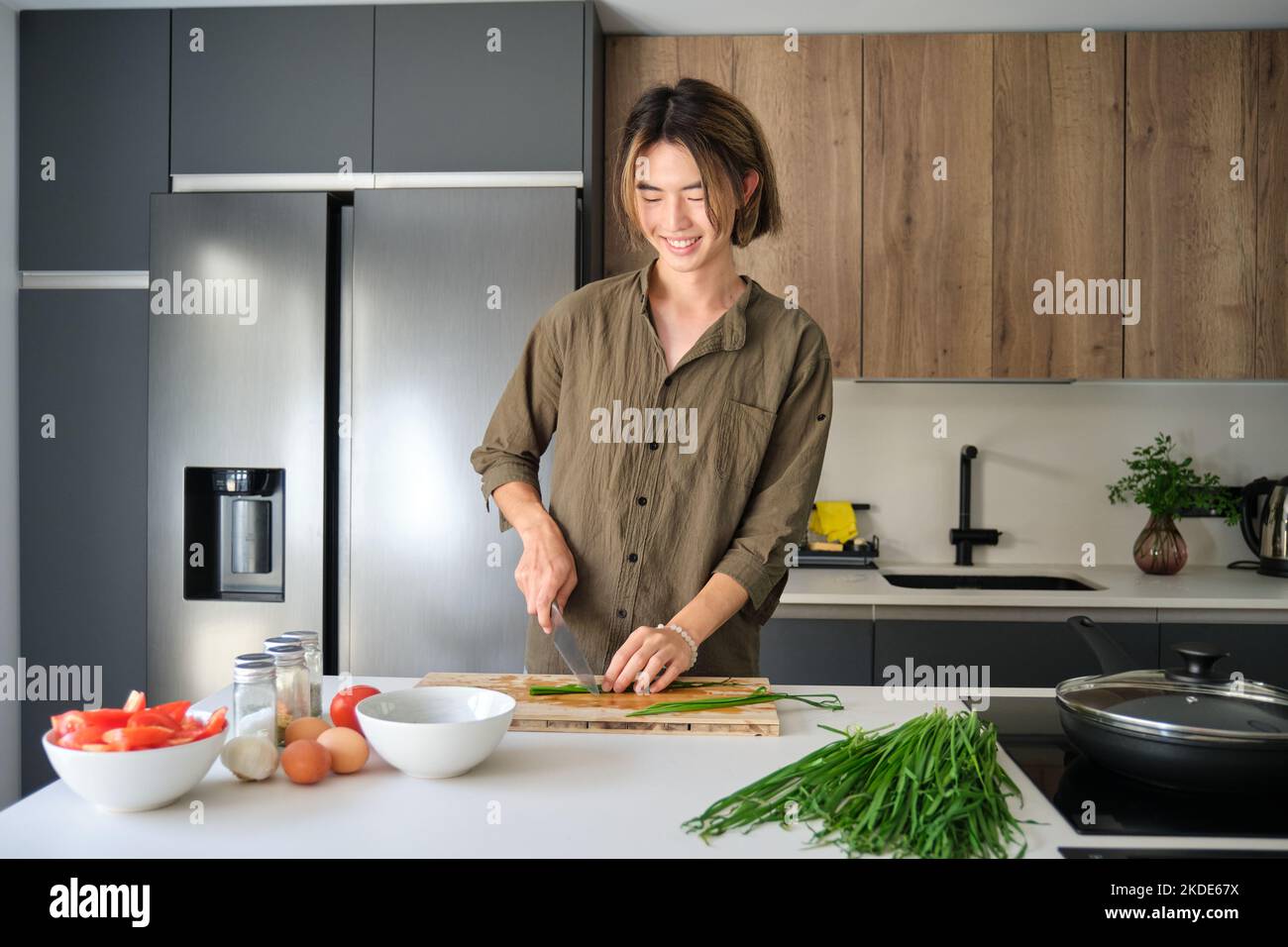 Giovane asiatico tagliare erba cipollina cinese in cucina. Foto Stock