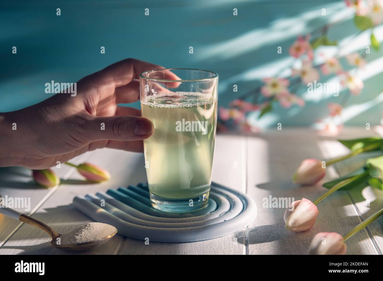 La mano della donna prende un bicchiere d'acqua con polvere di collagene matcha, sano e anti-età concetto Foto Stock