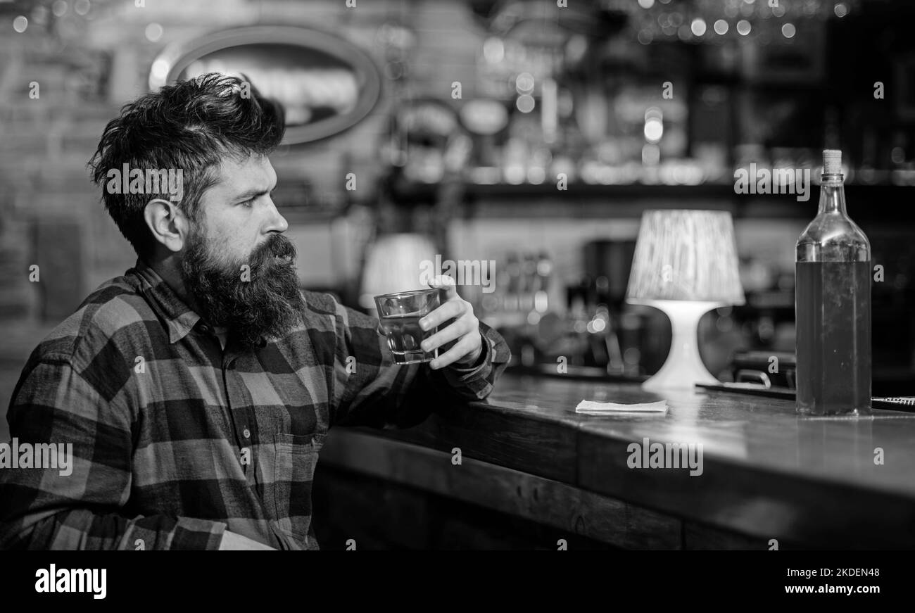 Ragazzo trascorrere il tempo libero al bar, sfondo sfocato. Hippster con barba ha ordinato una bottiglia piena di alcol. Concetto di relax. L'uomo beve whisky o cognac Foto Stock