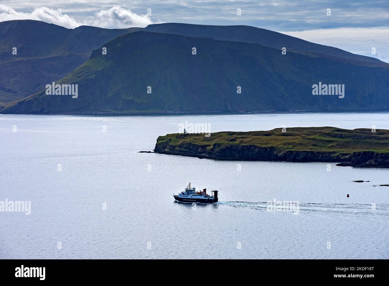 Il traghetto delle piccole isole MacBrayne della Caledonia, il MV Lochnevis, che lascia il porto, l'isola di canna, Scozia, REGNO UNITO. Le montagne di Rum dietro. Foto Stock