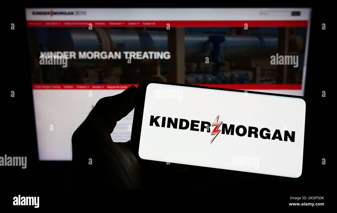 Persona che tiene il cellulare con il logo della società americana di energia Kinder Morgan Inc. Sullo schermo di fronte al sito web aziendale. Messa a fuoco sul display del telefono. Foto Stock