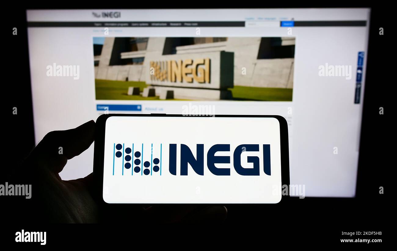 Persona che tiene il cellulare con il logo dell'agenzia di statistiche messicane INEGI sullo schermo di fronte alla pagina web. Messa a fuoco sul display del telefono. Foto Stock