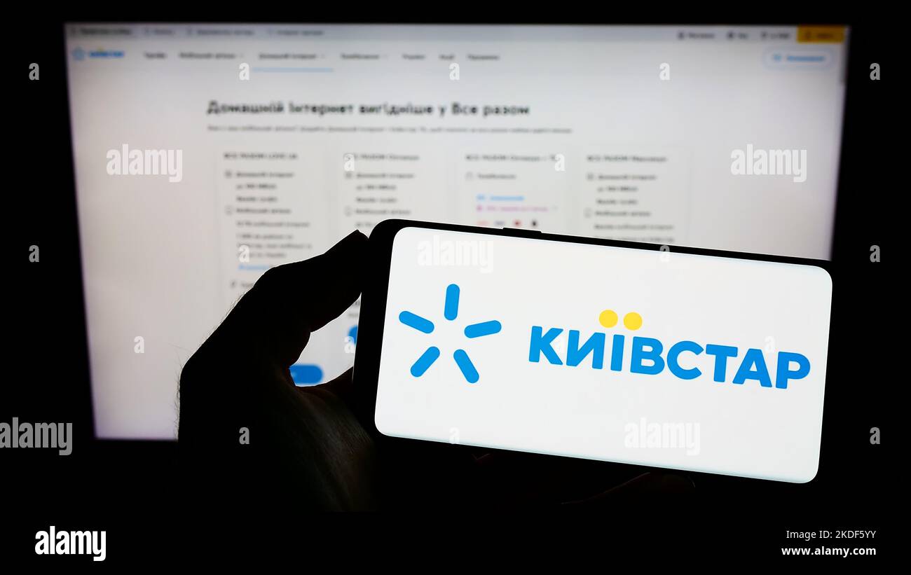 Persona che tiene il cellulare con il logo della società di telecomunicazioni Kyivstar JSC sullo schermo di fronte al sito web aziendale. Messa a fuoco sul display del telefono. Foto Stock