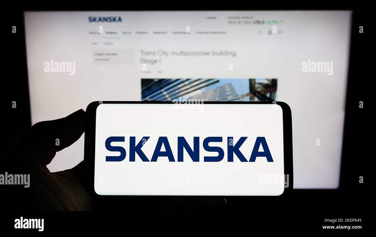 Persona che tiene uno smartphone con il logo della società svedese Skanska AB sullo schermo di fronte al sito Web. Messa a fuoco sul display del telefono. Foto Stock