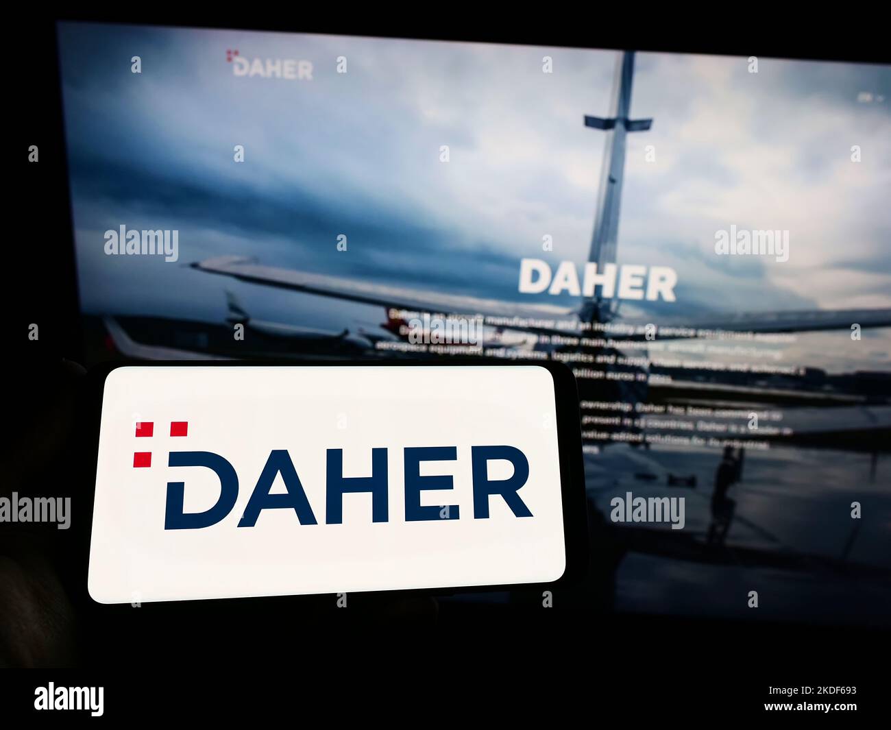 Persona che tiene uno smartphone con il logo della società aerospaziale francese Daher Group sullo schermo di fronte al sito Web. Messa a fuoco sul display del telefono. Foto Stock