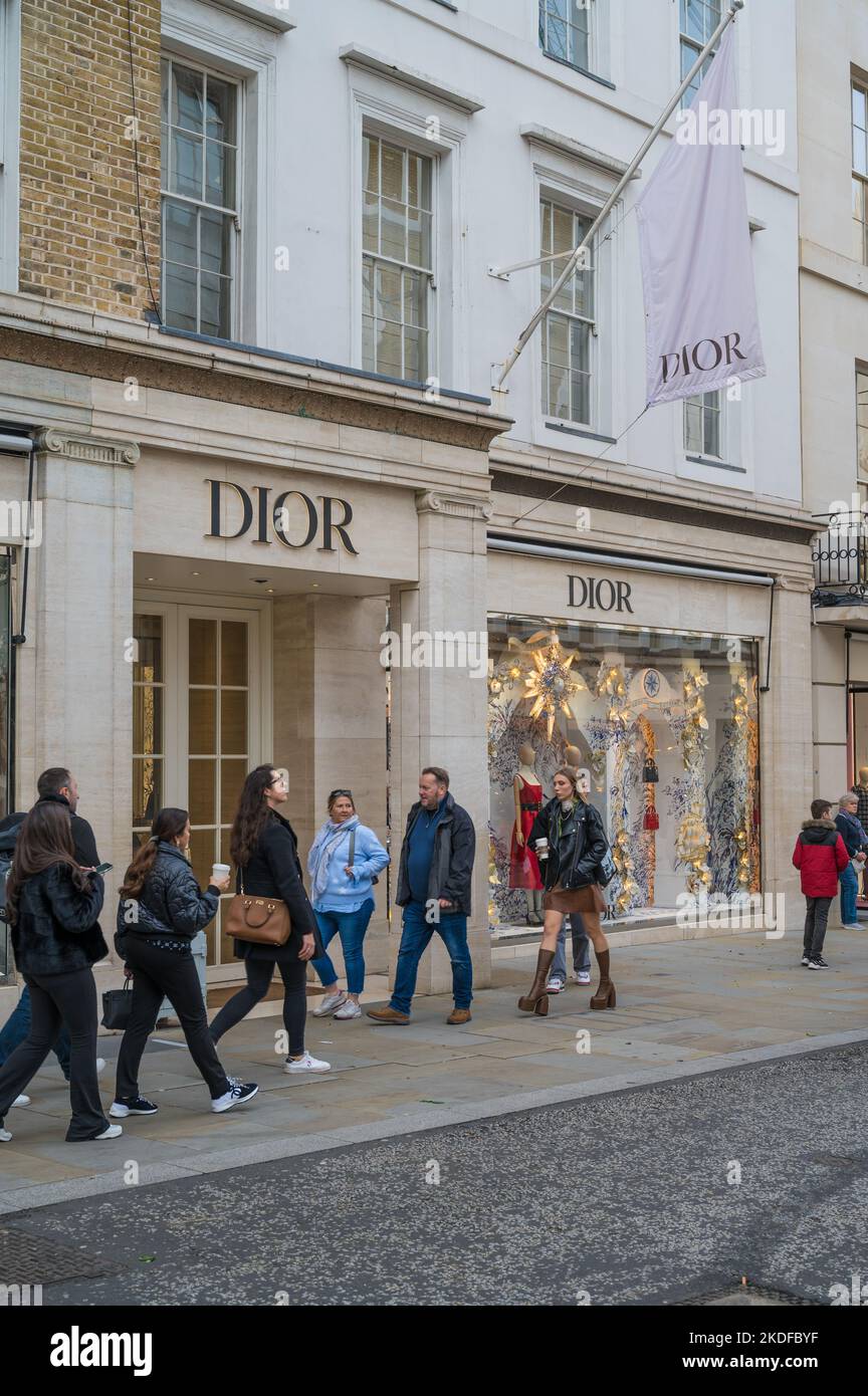 Le persone che si trovano in città per fare shopping passano dal negozio di moda Dior a New Bond Street, Mayfair, Londra, Inghilterra, Regno Unito Foto Stock