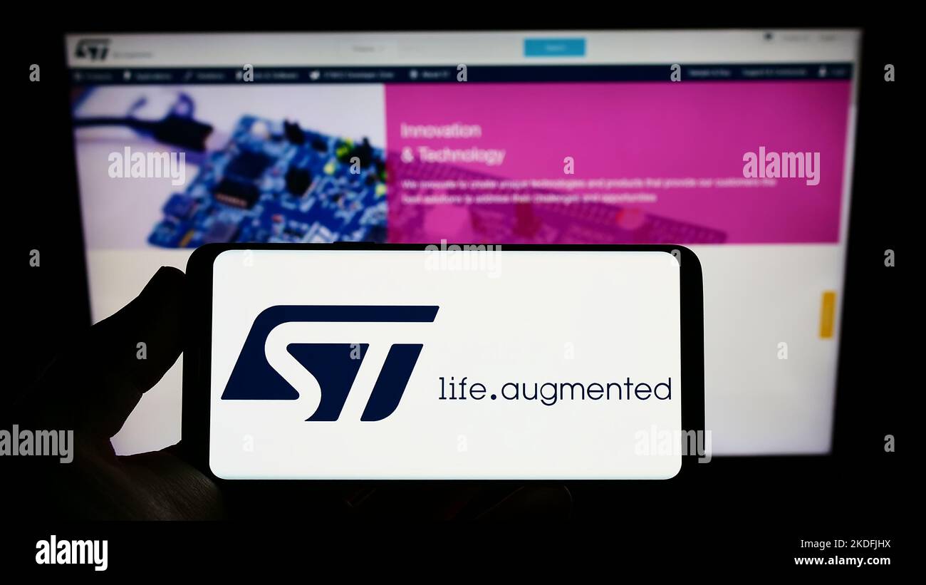 Persona che tiene uno smartphone con il logo della società di semiconduttori STMicroelectronics N.V. sullo schermo di fronte al sito Web. Messa a fuoco sul display del telefono. Foto Stock