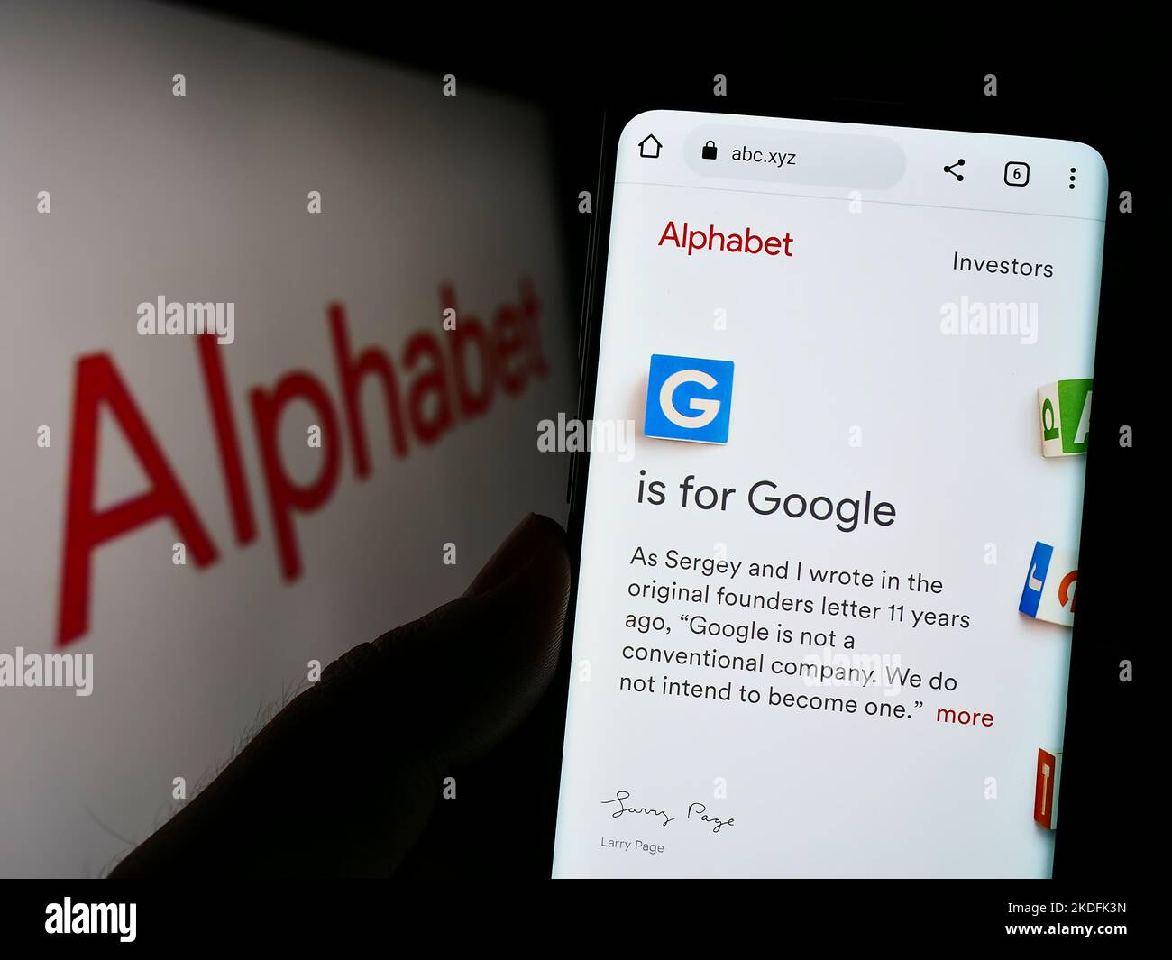 Persona che tiene il cellulare con la pagina web della holding americana Alphabet Inc. (Google) sullo schermo di fronte al logo. Messa a fuoco al centro del display del telefono. Foto Stock