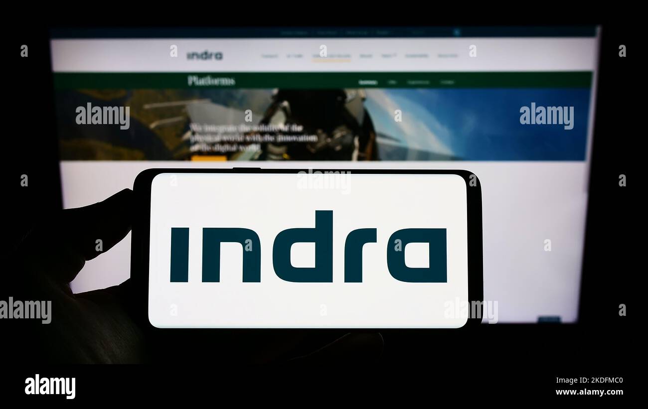 Persona che tiene uno smartphone con il logo della società spagnola Indra Sistemas S.A. sullo schermo di fronte al sito Web. Messa a fuoco sul display del telefono. Foto Stock