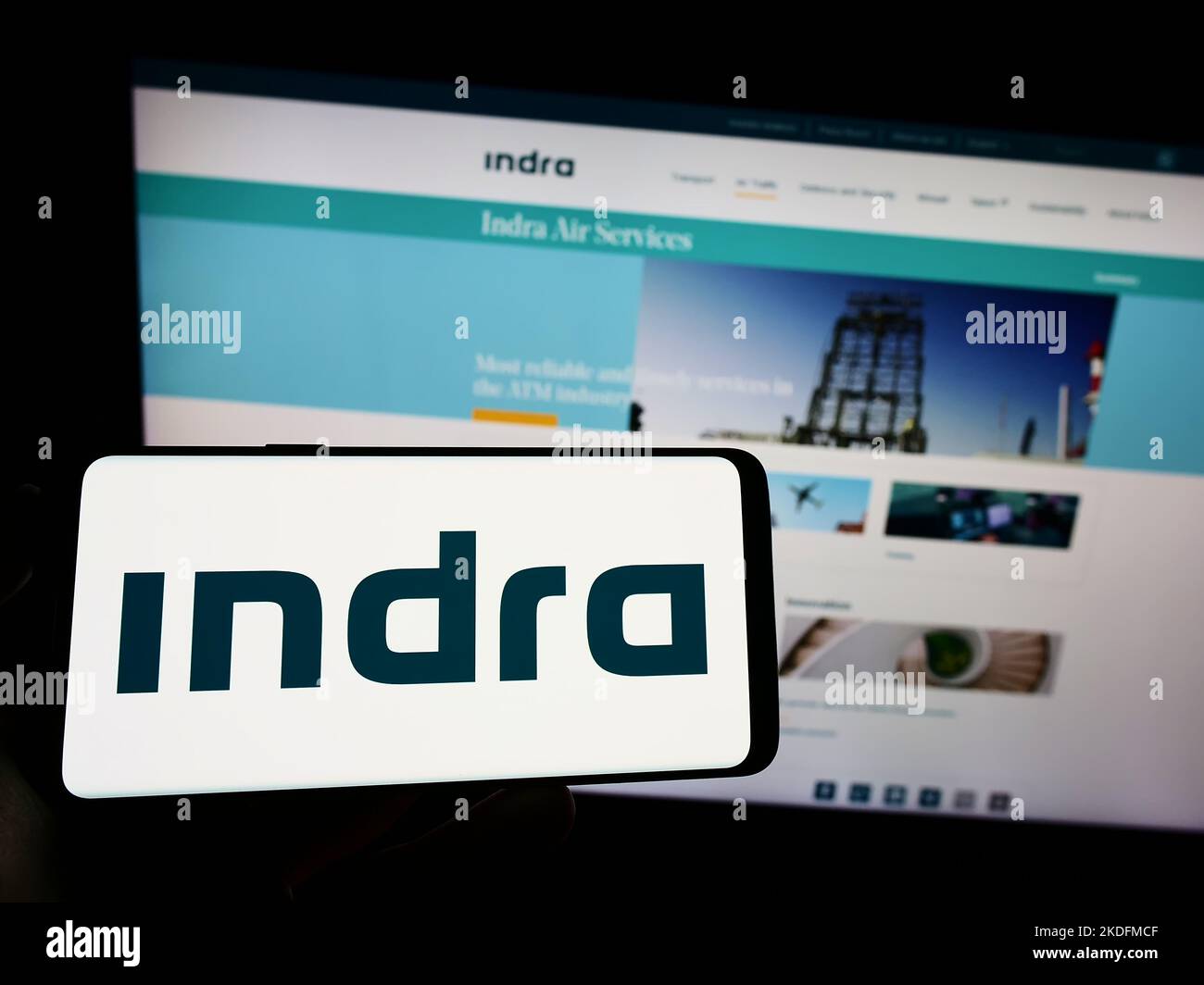 Persona che tiene il cellulare con il logo della società spagnola Indra Sistemas SA sullo schermo di fronte al sito web aziendale. Messa a fuoco sul display del telefono. Foto Stock