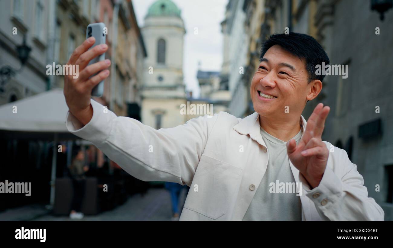 Gioioso adulto maschio in possesso di smartphone guardando lo schermo scattare foto sulla webcam felice uomo blogger posa per la fotografia utilizzando il telefono per Foto Stock