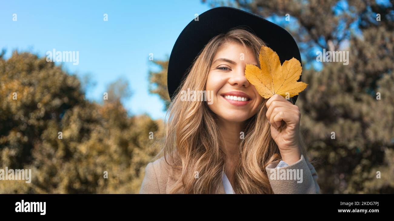 Giovane donna sorridente che copre il viso con una foglia gialla Foto Stock