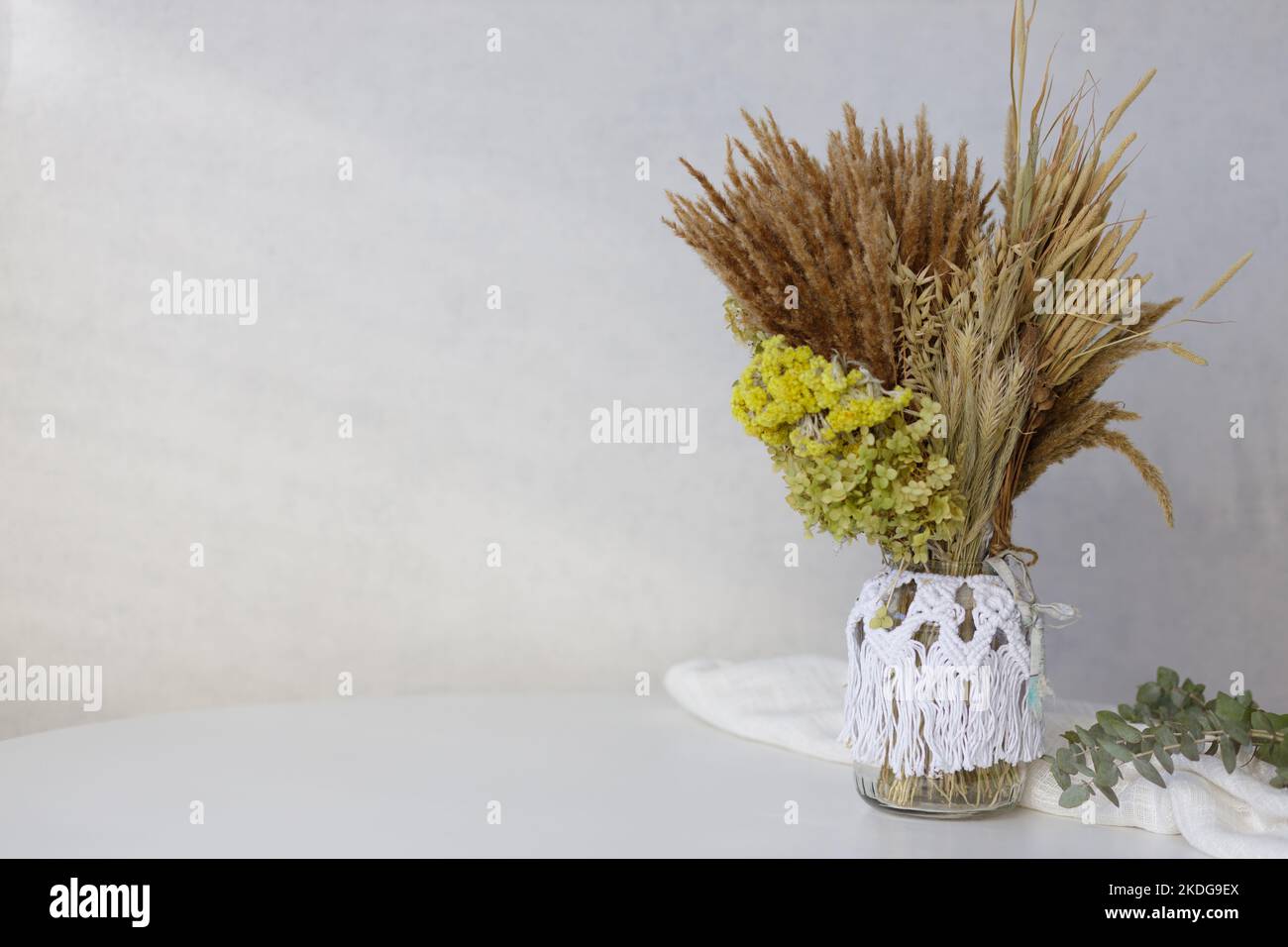 Sistemazione scandinava minimalista con fiori secchi in vaso macramato su un tavolo bianco Foto Stock