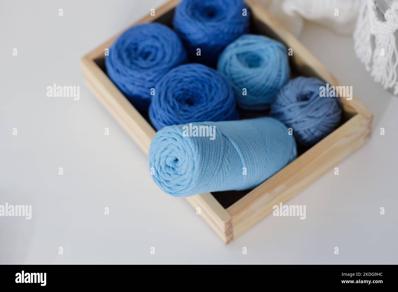 Palle di corde di macrame di cotone blu e azzurro in una scatola di legno su un tavolo bianco Foto Stock