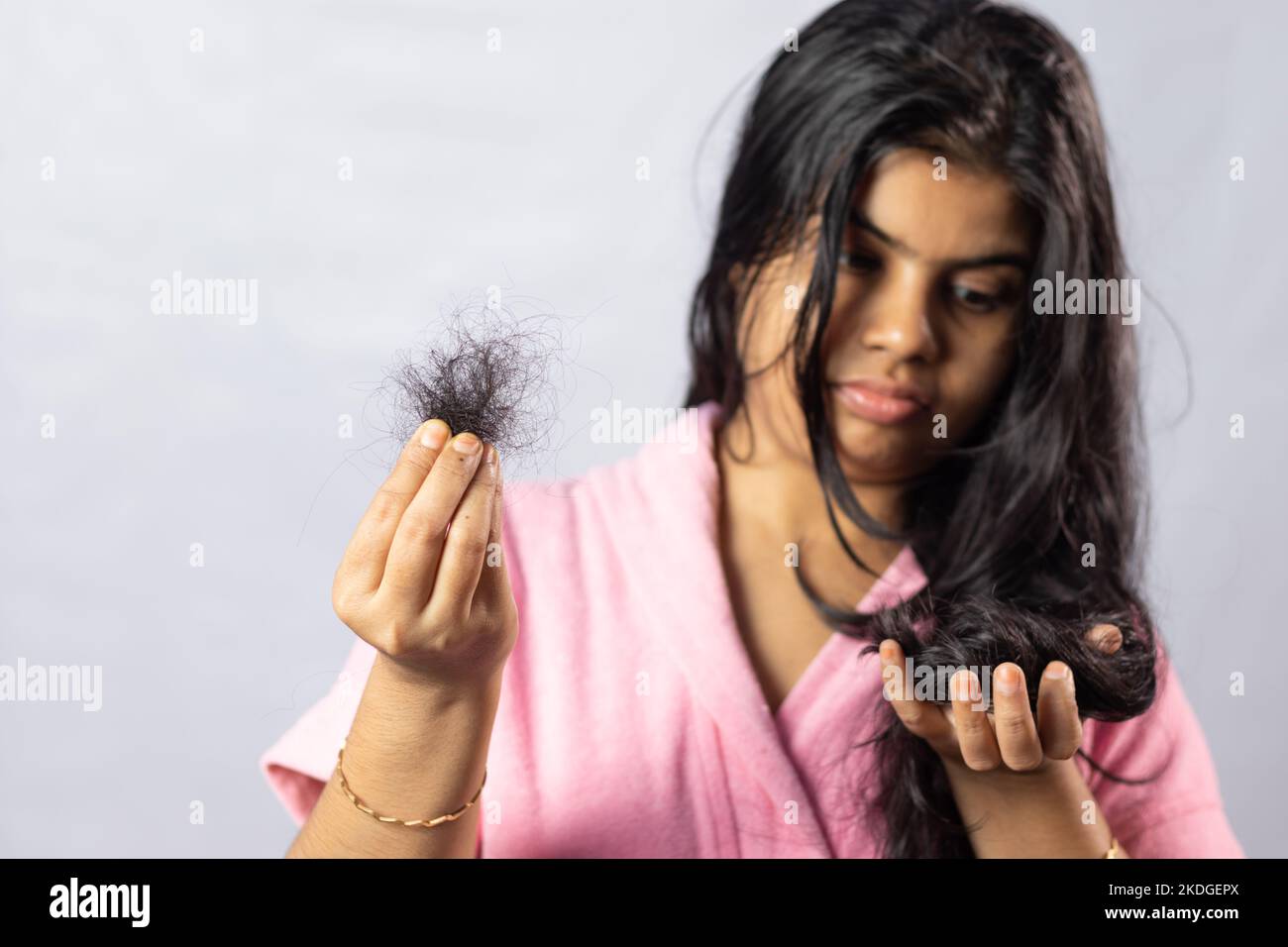 Fuoco selettivo sui capelli caduti tenuto in mano da una donna indiana preoccupata su sfondo bianco Foto Stock