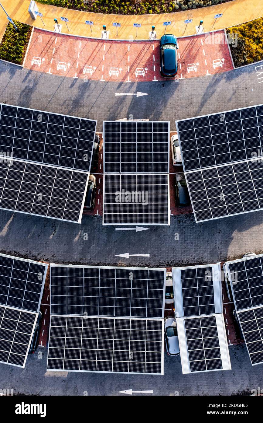 Vista aerea direttamente sopra auto elettriche parcheggio sotto pannelli solari su un parcheggio tetto pronto per la ricarica Foto Stock