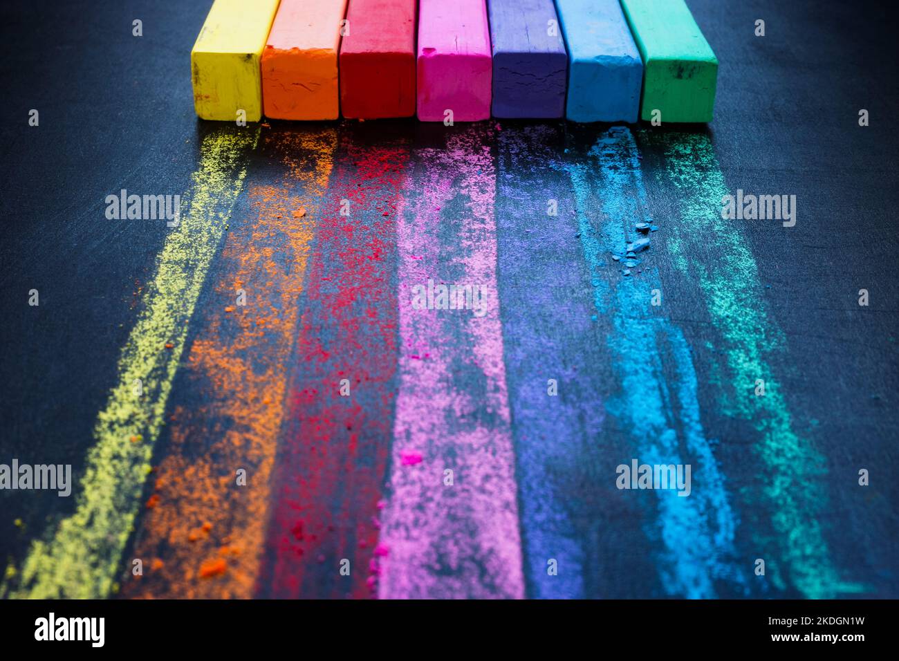 Pastelli colorati e un arcobaleno su una tavola nera. Concetto di unità e diversità. Foto Stock