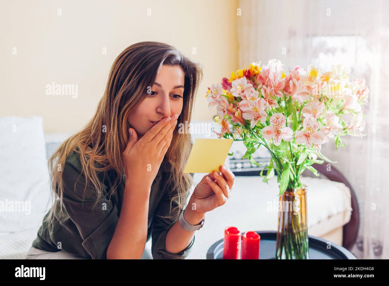 Sorpresa giovane donna legge la carta lasciata in mazzo di fiori dal ragazzo a casa. Presenta il regalo con una nota. Foto Stock