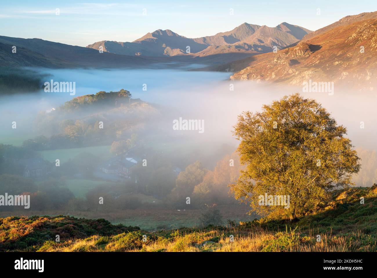 Mist in Dyffryn Mymbyr fornisce la separazione per un bellissimo albero autunnale sopra Capel Curig in Snowdonia, con lo Snowdon Horseshoe che incornicia la scena. Foto Stock