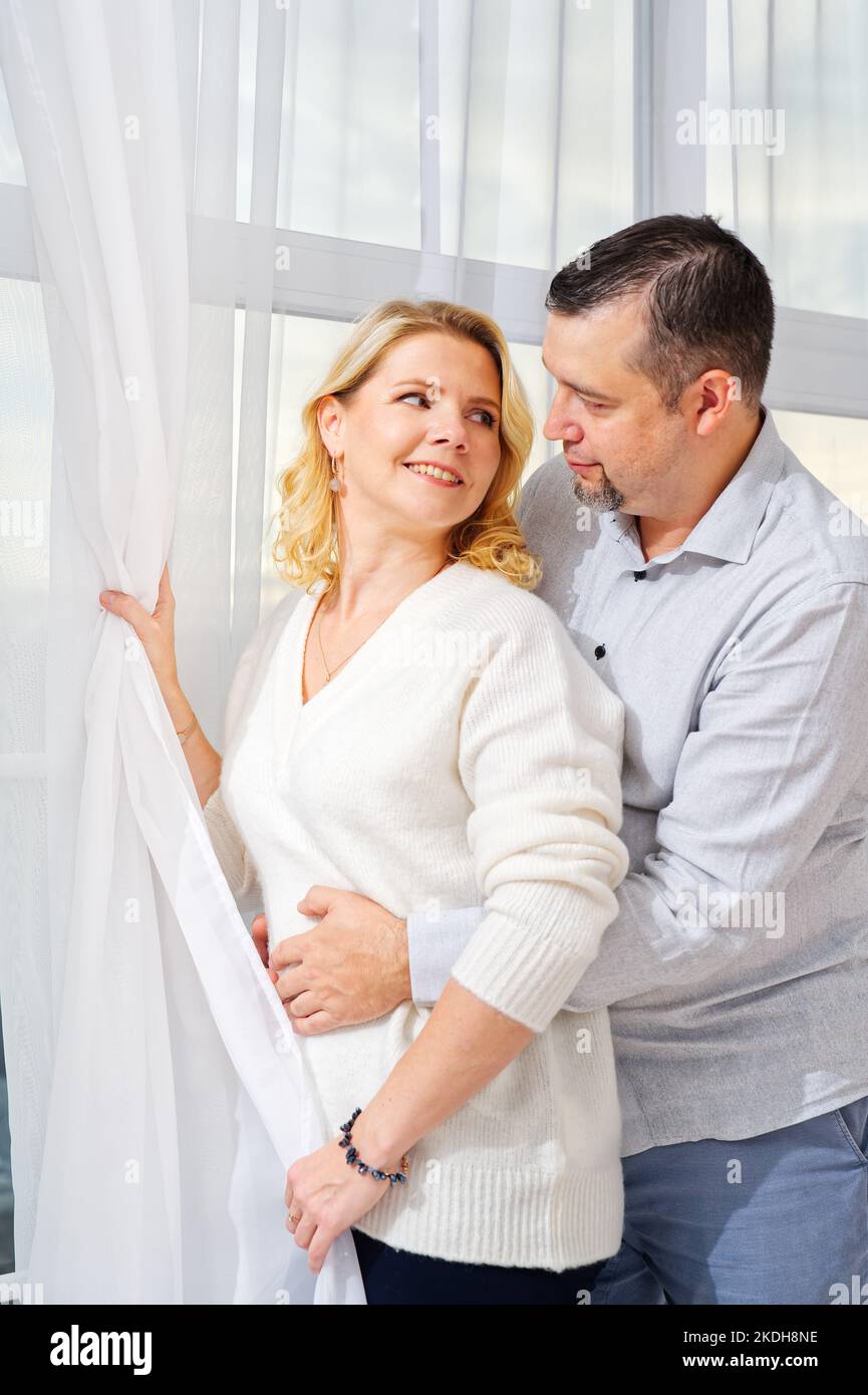 Coppia di mezza età che si abbraccia davanti alla finestra. Ritratto di donna e uomo bionda di mezza età Foto Stock