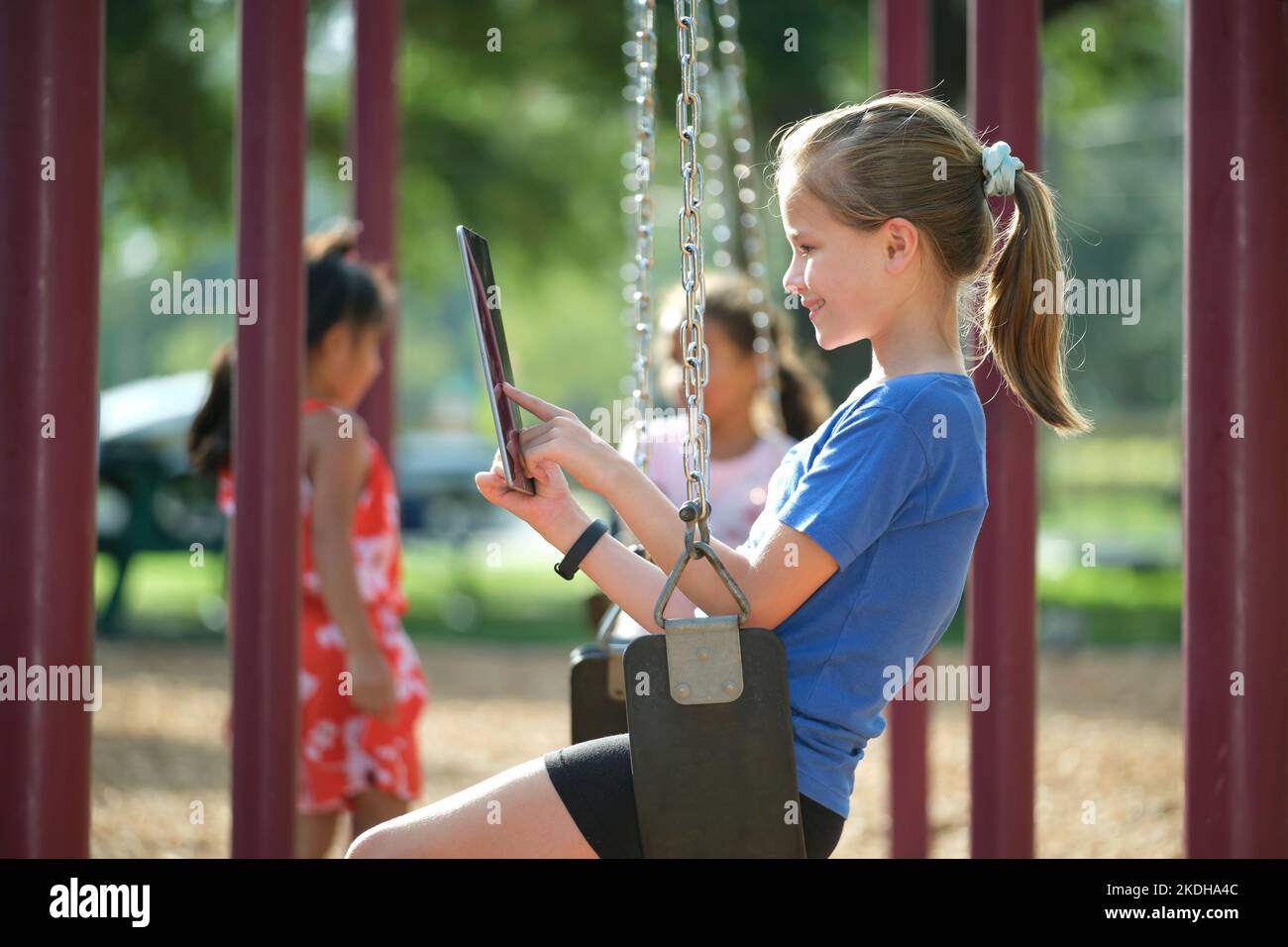 Ragazza felice bambino che utilizza un tablet digitale per giocare a videogame durante le vacanze estive seduto sul swing nel parco Foto Stock
