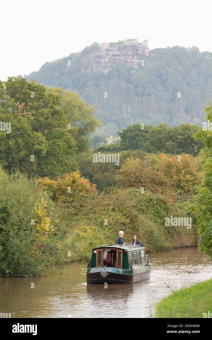 Una nave da crociera che navighi sul canale Shropshire Union in autunno con le Crags rocciose del Castello di Beeston, Cheshire, sullo sfondo Foto Stock