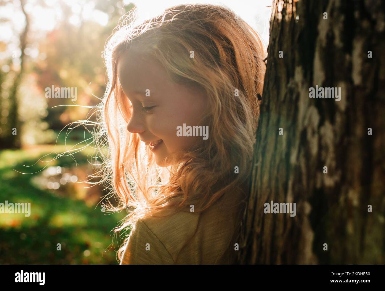 ritratto di ragazza che gioca a nascondersi e cercare dietro un albero al tramonto Foto Stock