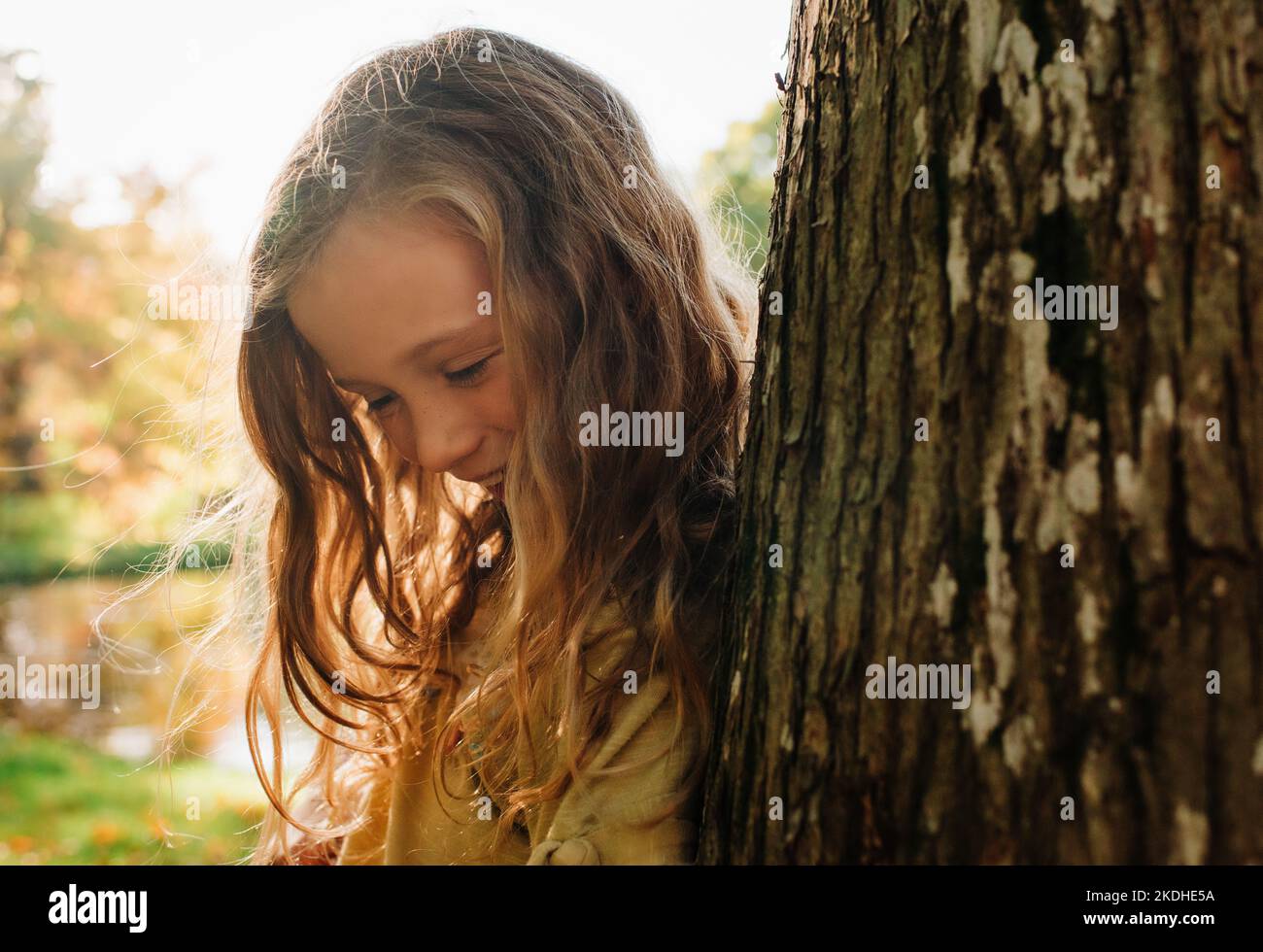 primo piano ritratto di bella ragazza nascosta da un albero in luce dorata Foto Stock