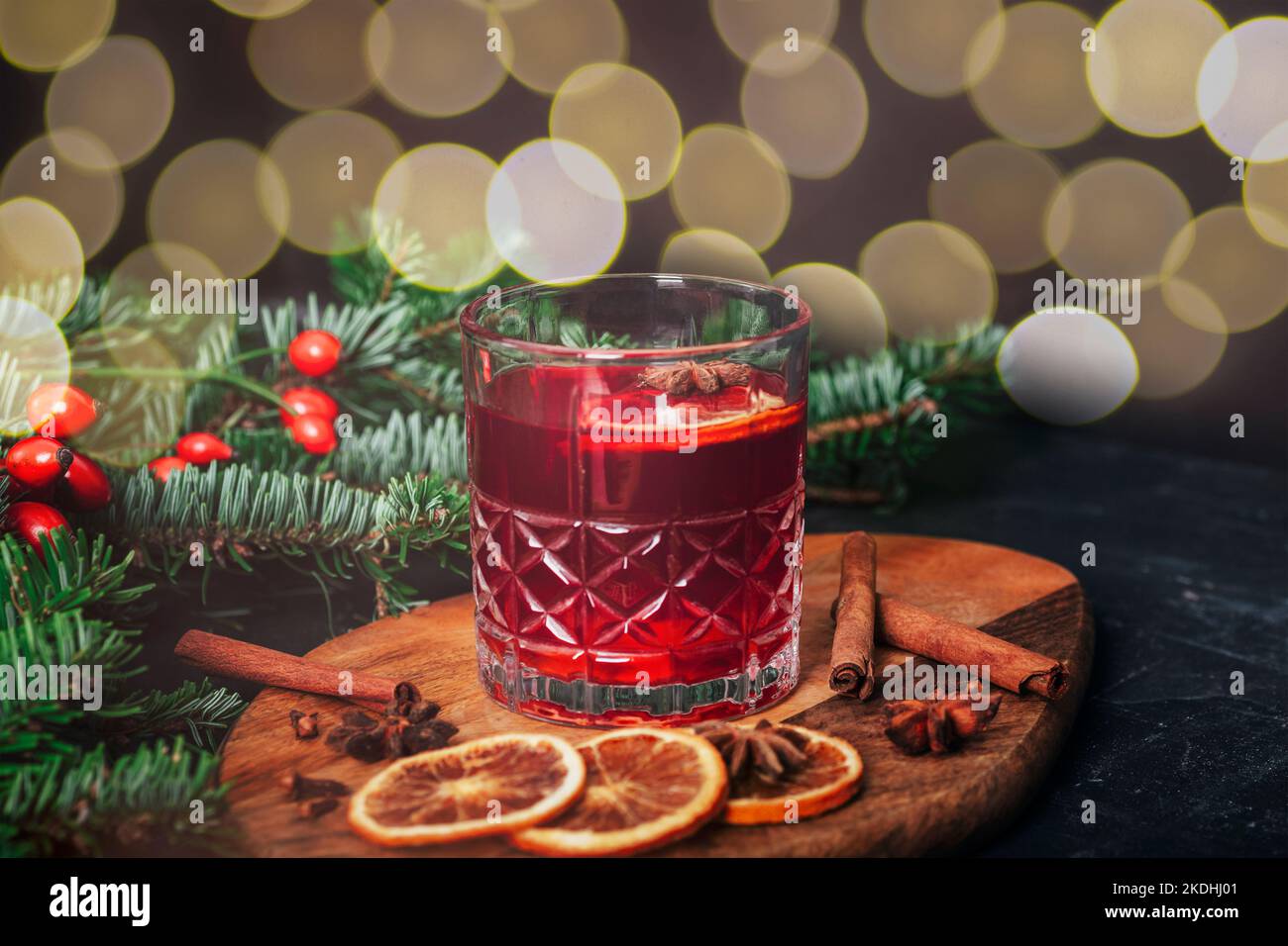 VIN brulé in un bicchiere su tagliere di legno con spezie, rametto di abete rosso e bokeh sullo sfondo, primo piano. Foto Stock