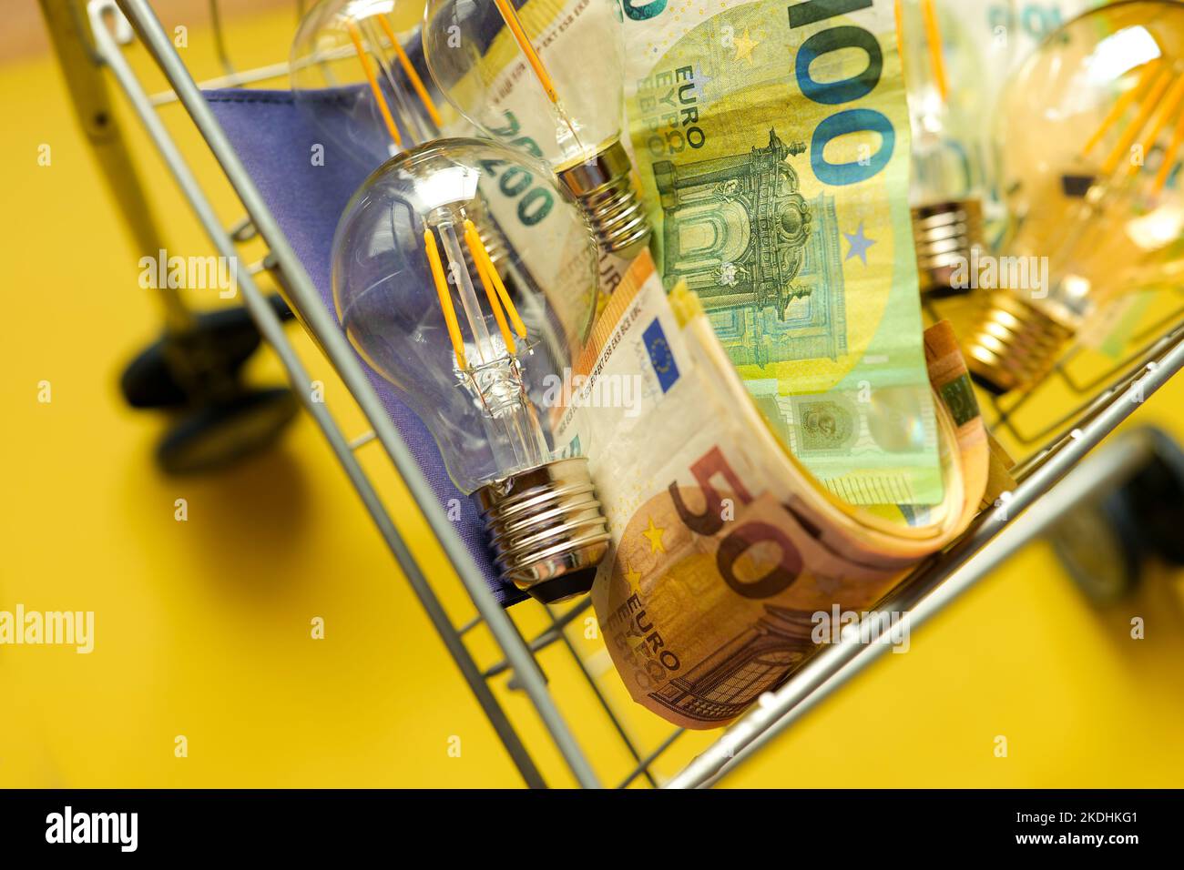 Lampadine e banconote in euro in un carrello supermercato su sfondo giallo.crisi nel settore dell'energia. Foto Stock