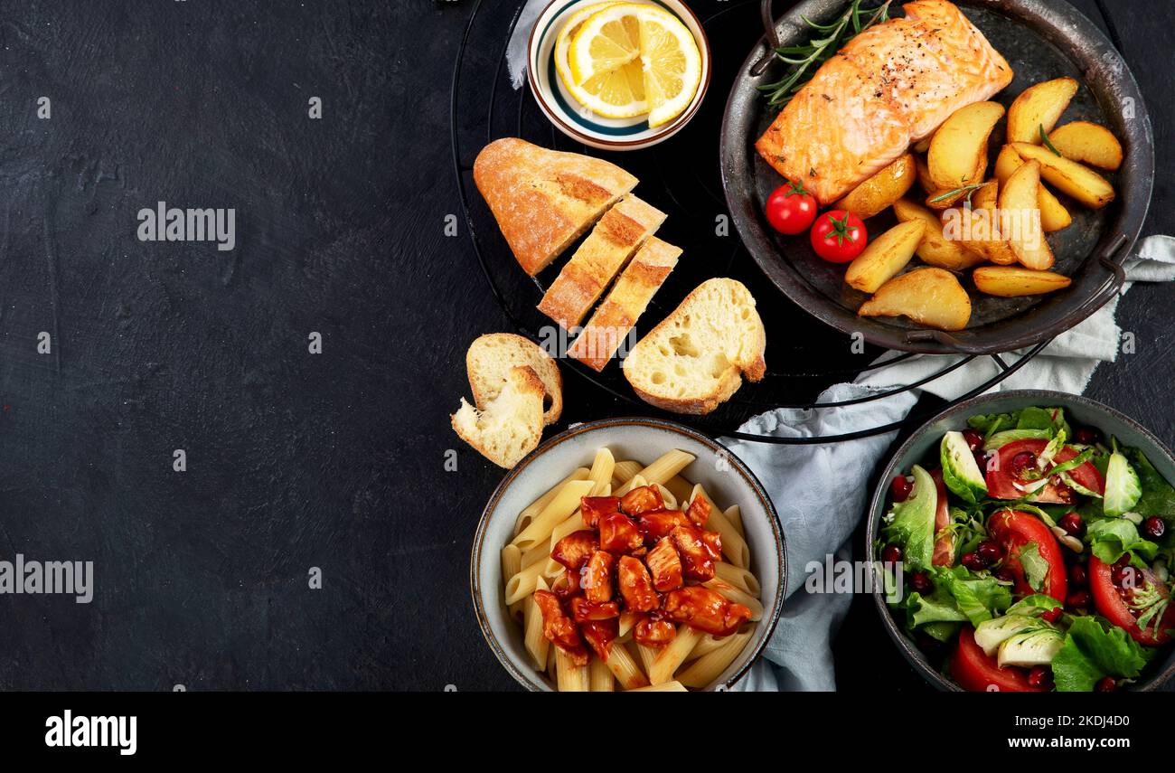 Set di vari piatti principali. Diversi piatti salutari, piatti di carne e pesce, pasta, insalate, salse, pane e verdure su sfondo scuro. Da a. Foto Stock