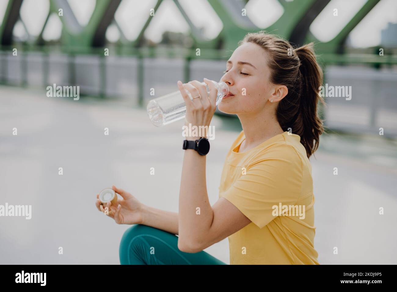Giovane donna che beve acqua durante il jogging in città, stile di vita sano e concetto di sport. Foto Stock