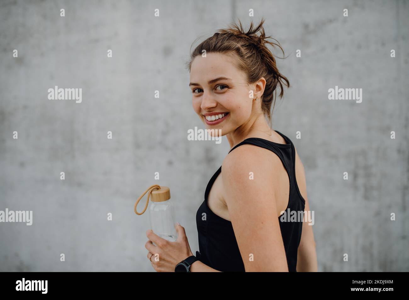 Giovane donna che beve acqua durante il jogging in città, stile di vita sano e concetto di sport. Foto Stock