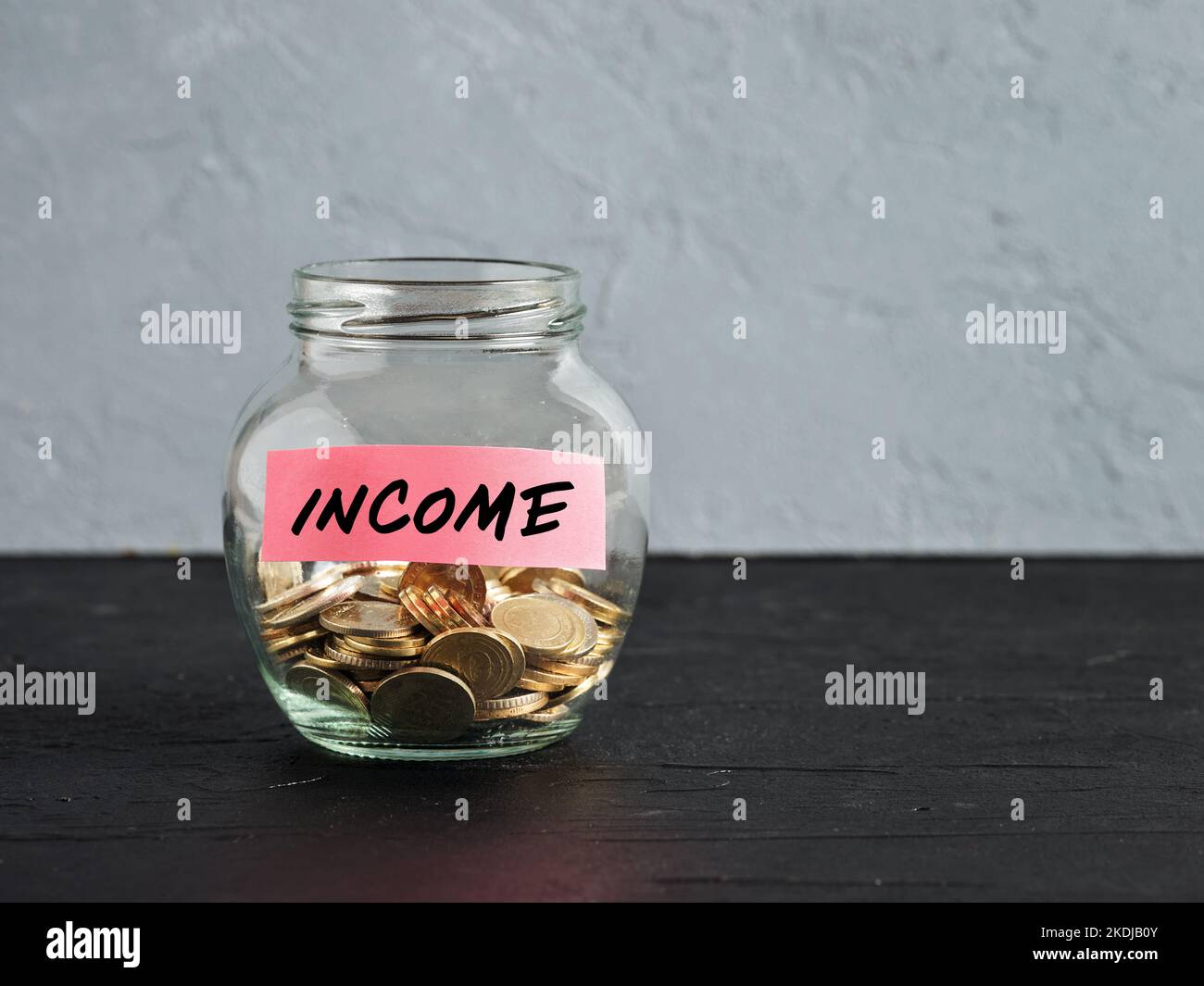 Vasetto di vetro con monete e la parola reddito su un'etichetta. Risparmio, investimento, raccolta di denaro reddito o suggerimenti concetti. Foto Stock