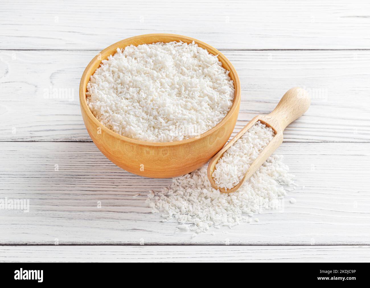 Scaglie di cocco in recipiente di legno con paletta su fondo di legno bianco Foto Stock